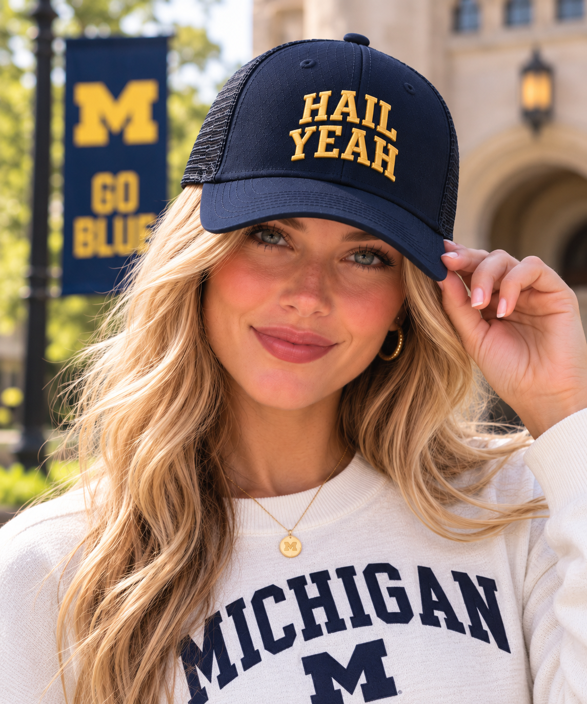 Blonde woman wearing the navy University of Michigan Honey Lid trucker hat with maize HAIL YEAH puff embroidery on campus