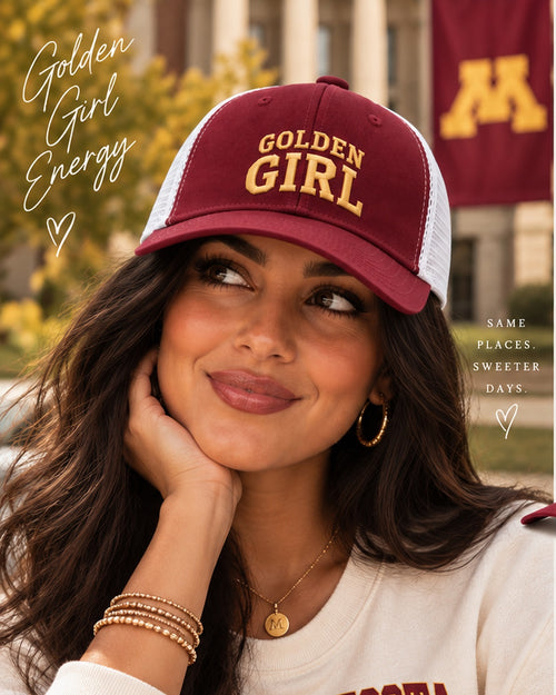 Female model wearing the Honey Lid maroon and white low-profile trucker with gold Golden Girl embroidery on the University of Minnesota campus