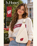 Campus model wearing the Honey Sling: University of Wisconsin — ivory canvas sling bag with the red Motion W and antique gold hardware